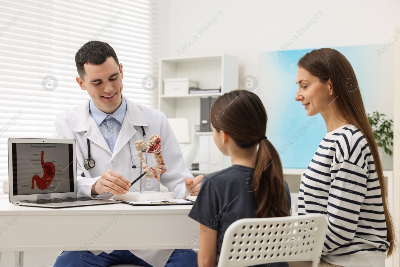 Photo of Gastroenterologist with model of intestine consulting woman and her daughter in clinic