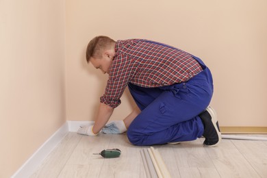 Photo of Man installing plinth on laminated floor in room