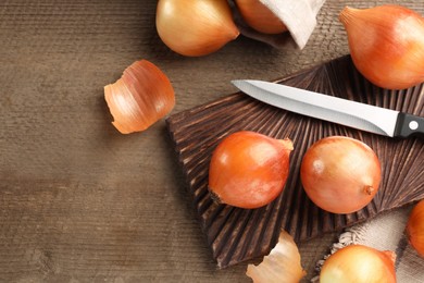 Many ripe onions and knife on wooden table, flat lay
