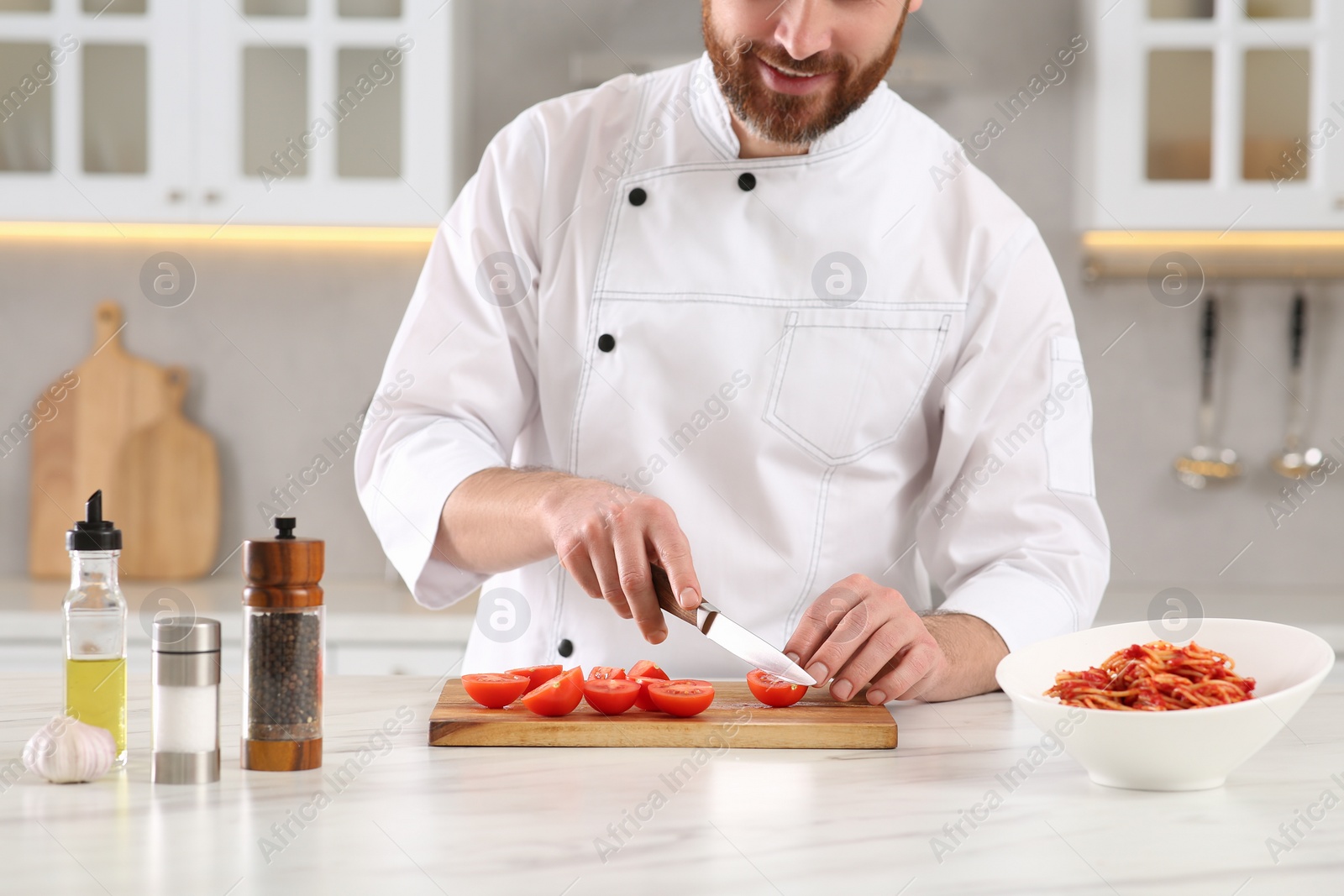 Photo of Professional chef cutting tomatoes for delicious spaghetti at marble table in kitchen, closeup