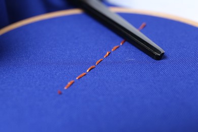 Photo of Stitches and scissors on blue cloth, closeup