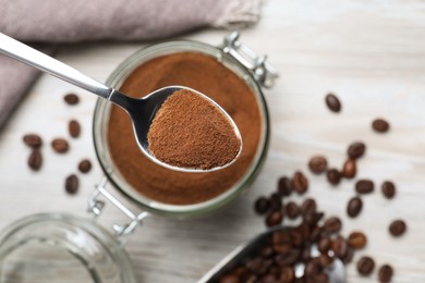 Spoon of instant coffee over jar on white table, top view