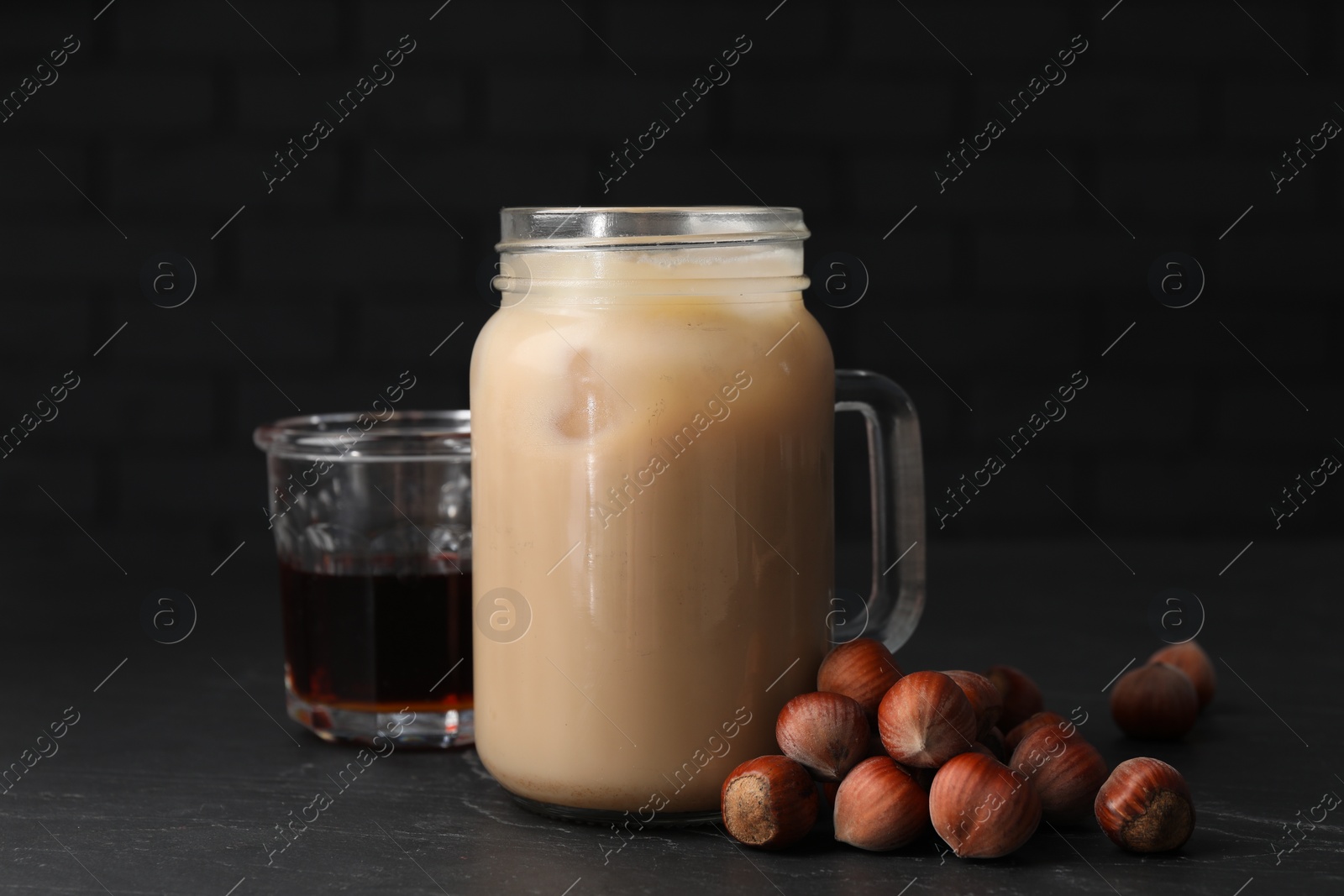 Photo of Mason jar of delicious iced coffee, syrup and hazelnuts on black table