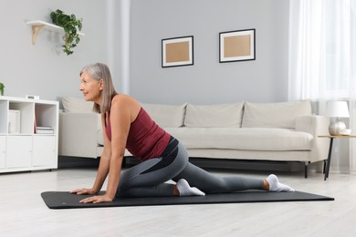 Photo of Senior woman in sportswear stretching on fitness mat at home
