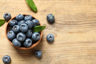 Bowl of tasty fresh blueberries and green leaves on wooden table, flat lay. Space for text