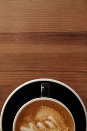 Cup of fresh aromatic coffee on wooden table, top view