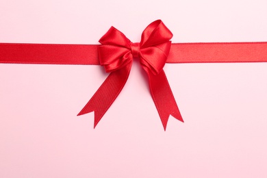 Photo of Red ribbon with bow on color background, top view