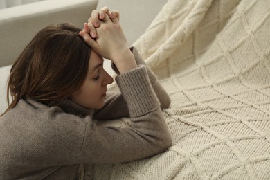 Photo of Sad young woman sitting near sofa at home, space for text