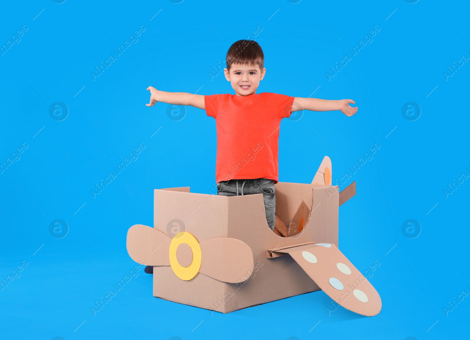 Photo of Cute little child playing with cardboard airplane on light blue background