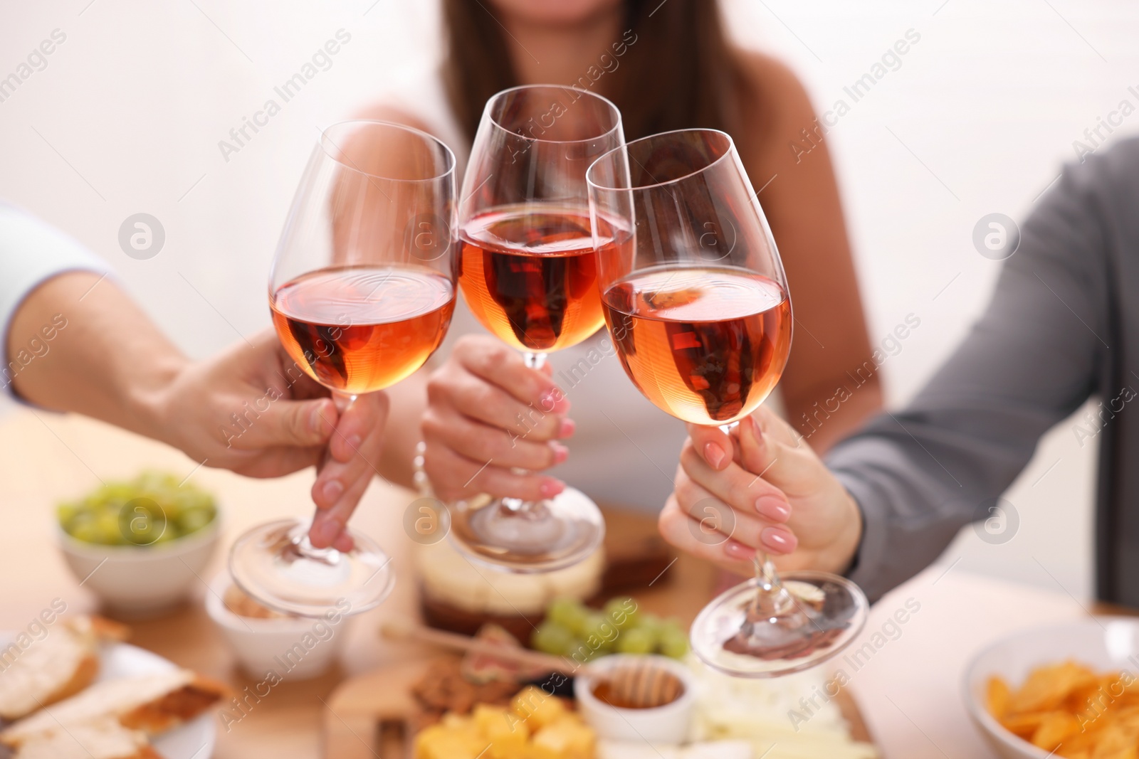 Photo of People clinking glasses with rose wine above wooden table, closeup