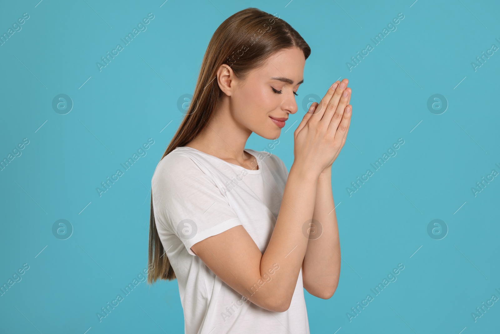 Photo of Woman with clasped hands praying on turquoise background