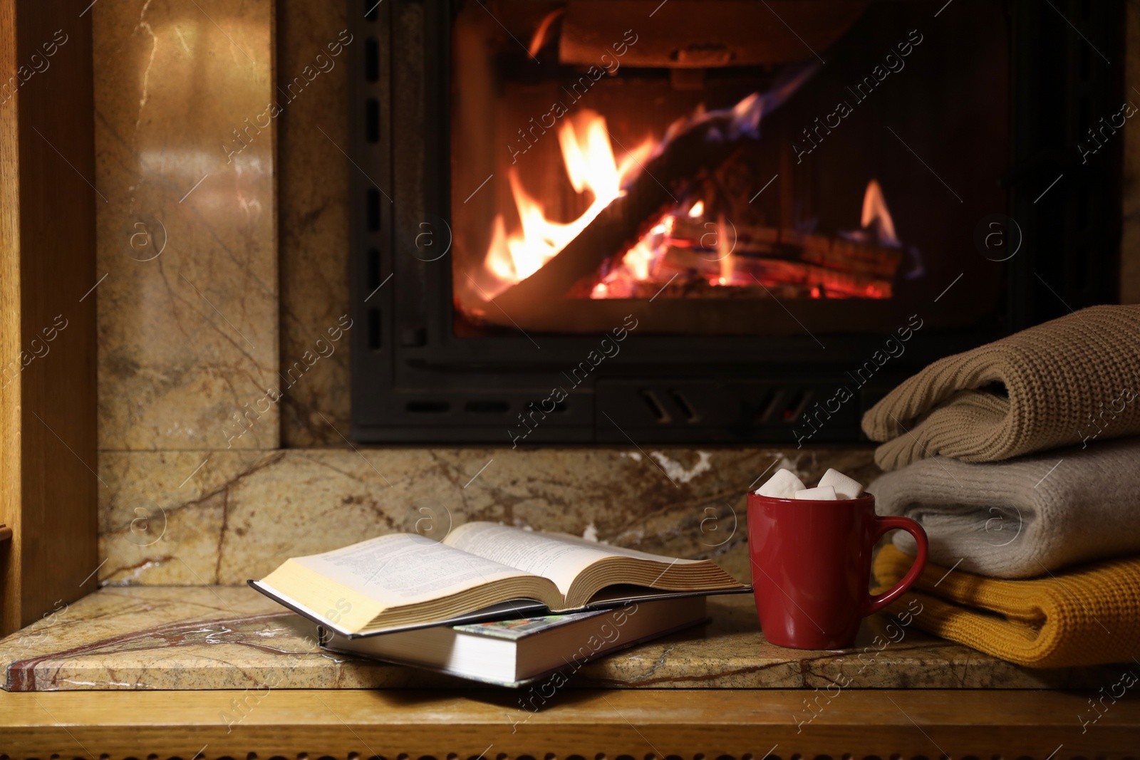 Photo of Stack of warm sweaters, cup, books and fireplace indoors