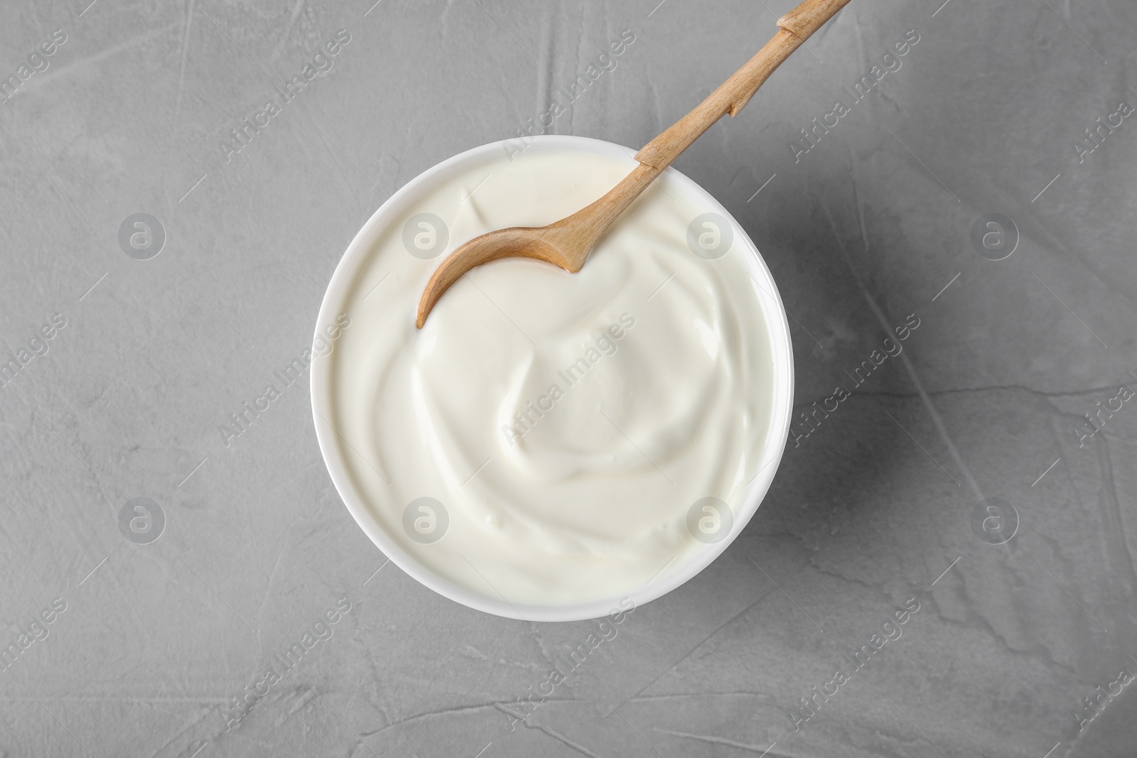 Photo of Bowl of sour cream with wooden spoon on grey table, flat lay