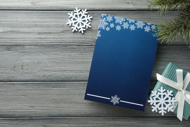 Blank Christmas invitation card, gift box, fir tree branches and decorative snowflakes on grey wooden table, flat lay. Space for text