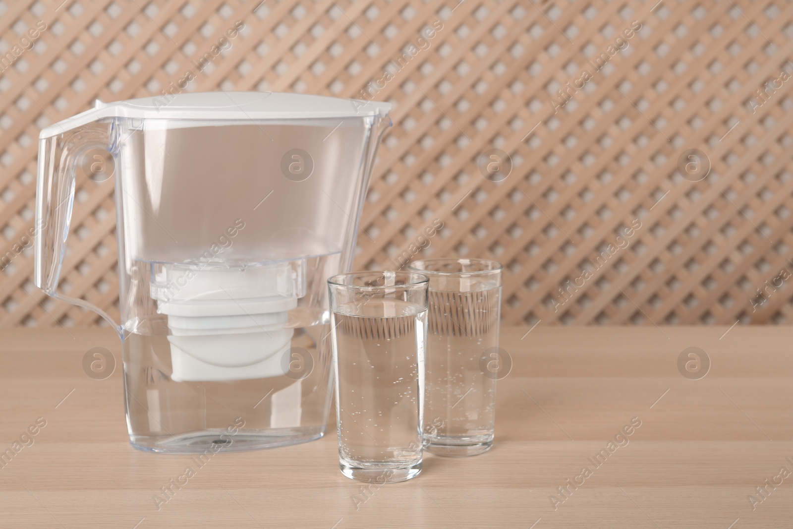 Photo of Filter jug and glasses with purified water on wooden table indoors. Space for text