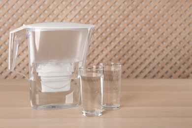 Photo of Filter jug and glasses with purified water on wooden table indoors. Space for text