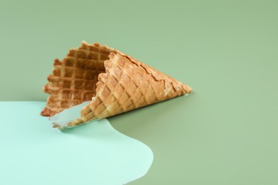Photo of Melted ice cream and wafer cone on green background, closeup. Space for text