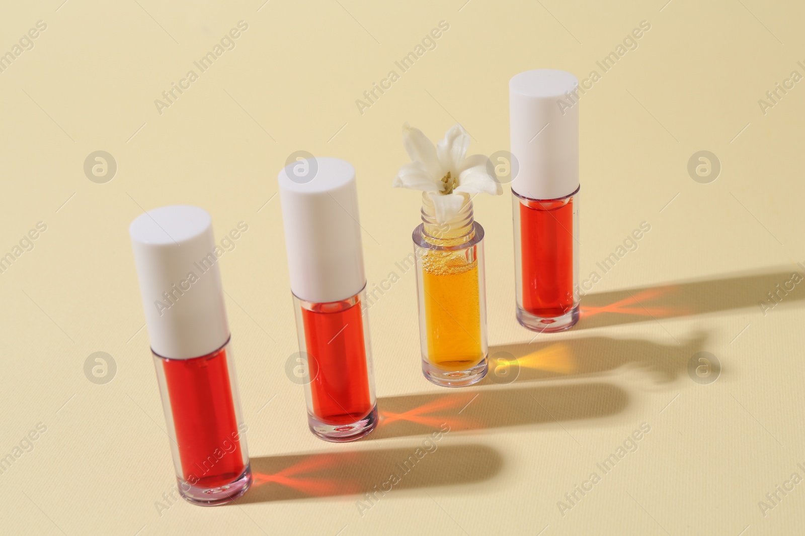 Photo of Bright lip glosses and flower on beige background
