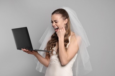 Cheerful bride with laptop on gray background