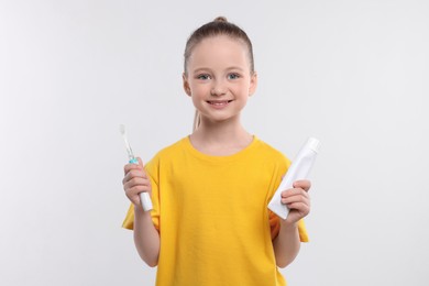 Photo of Happy girl holding electric toothbrush and tube of toothpaste on white background