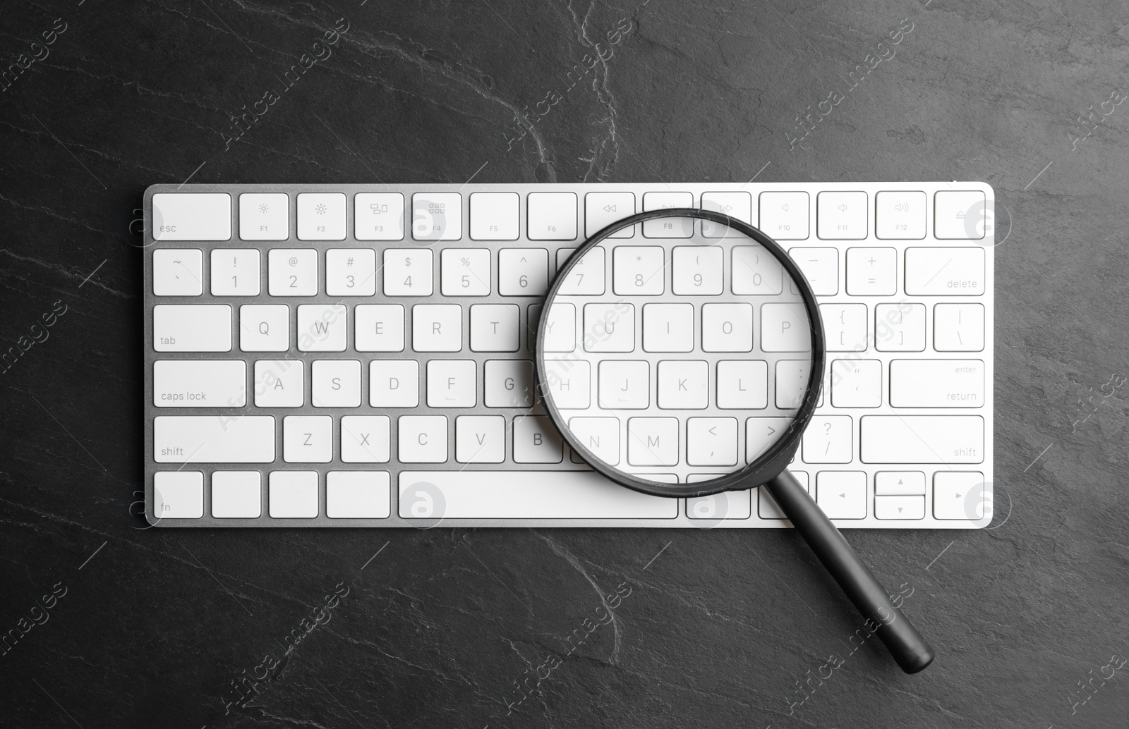 Photo of Magnifier glass and keyboard on black slate background, flat lay. Find keywords concept