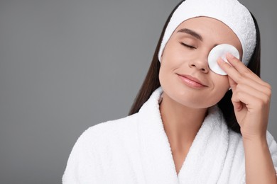 Photo of Young woman cleaning her face with cotton pad on grey background. Space for text