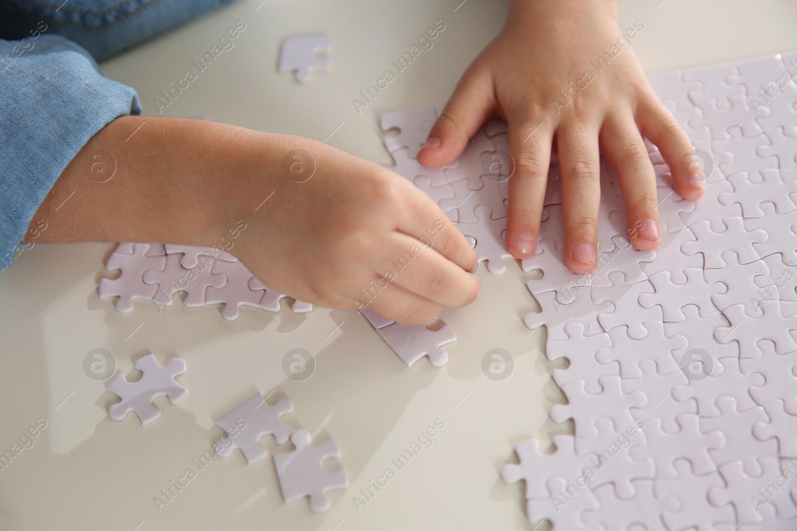 Photo of Little girl playing with puzzles at table, closeup