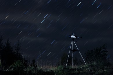 Modern telescope and beautiful sky in night outdoors. Star trail