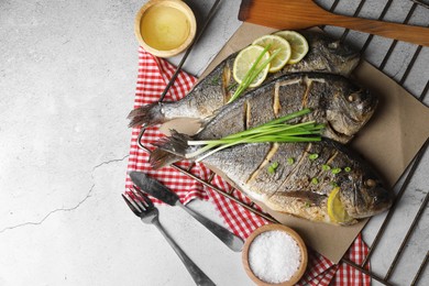 Seafood. Delicious baked fish served with green onion and lemon on light textured table, flat lay. Space for text