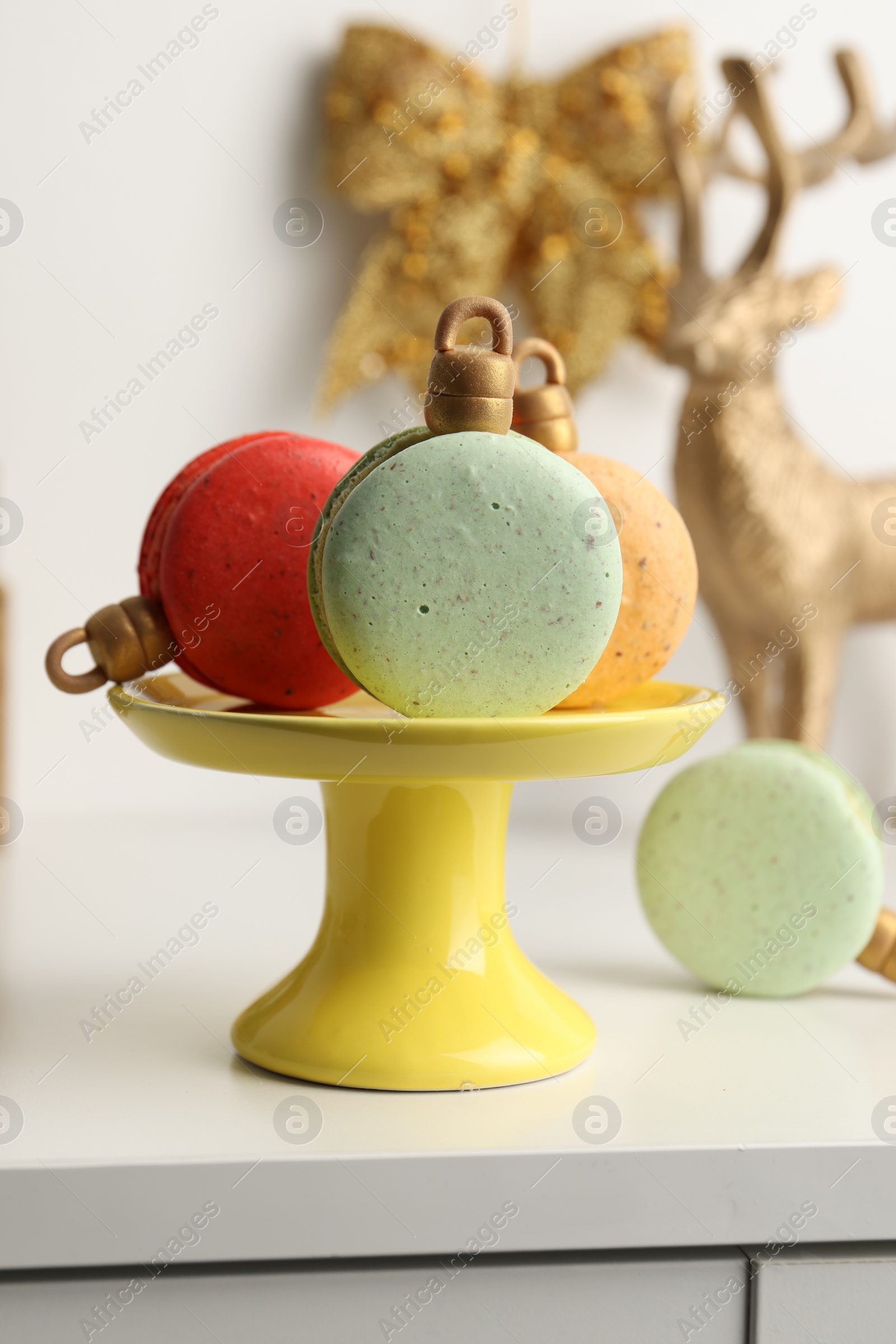 Photo of Stand with beautifully decorated Christmas macarons on white table