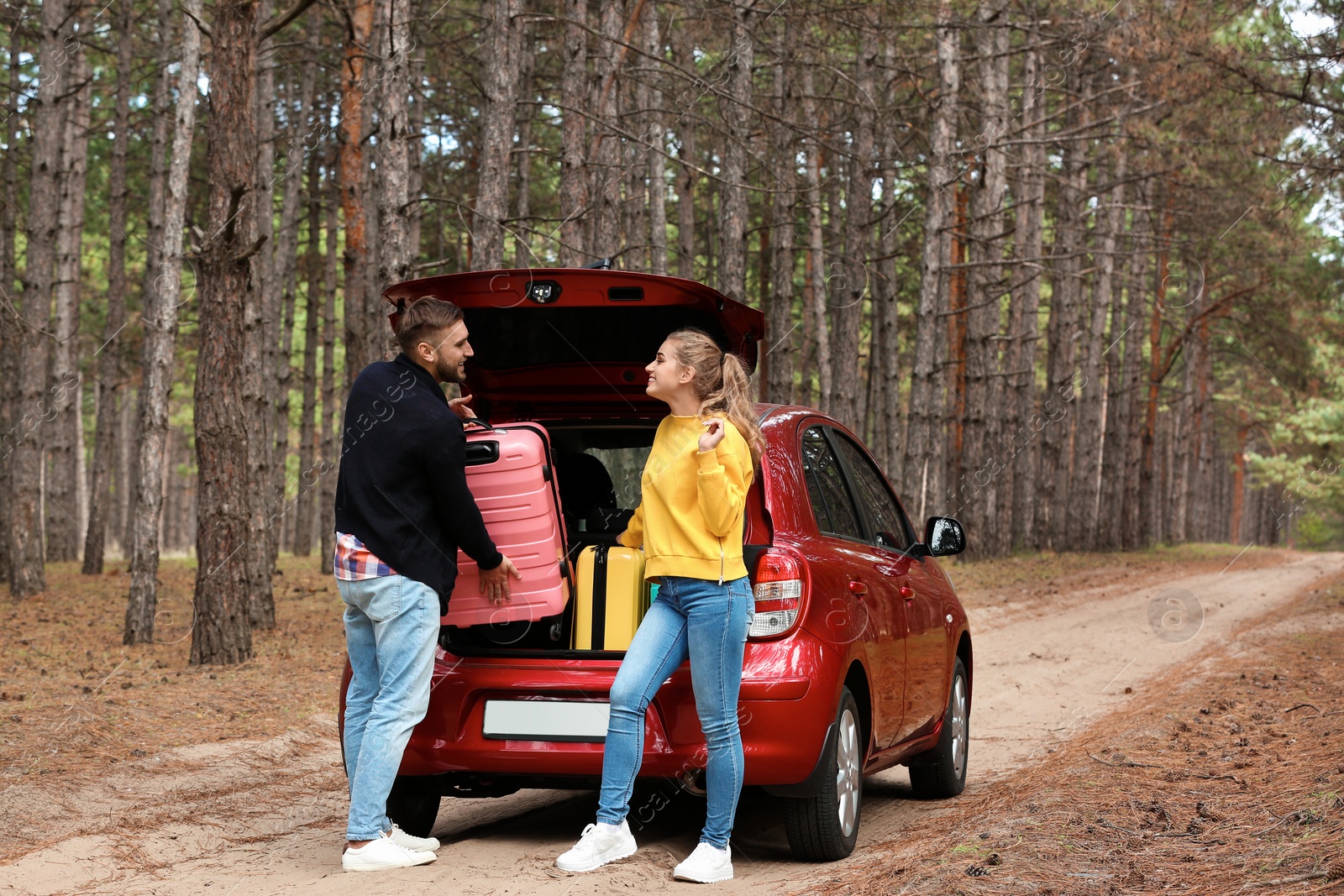 Photo of Young couple loading suitcases into car trunk on forest road