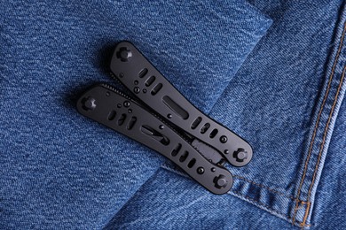 Photo of Modern compact portable multitool on denim fabric, top view