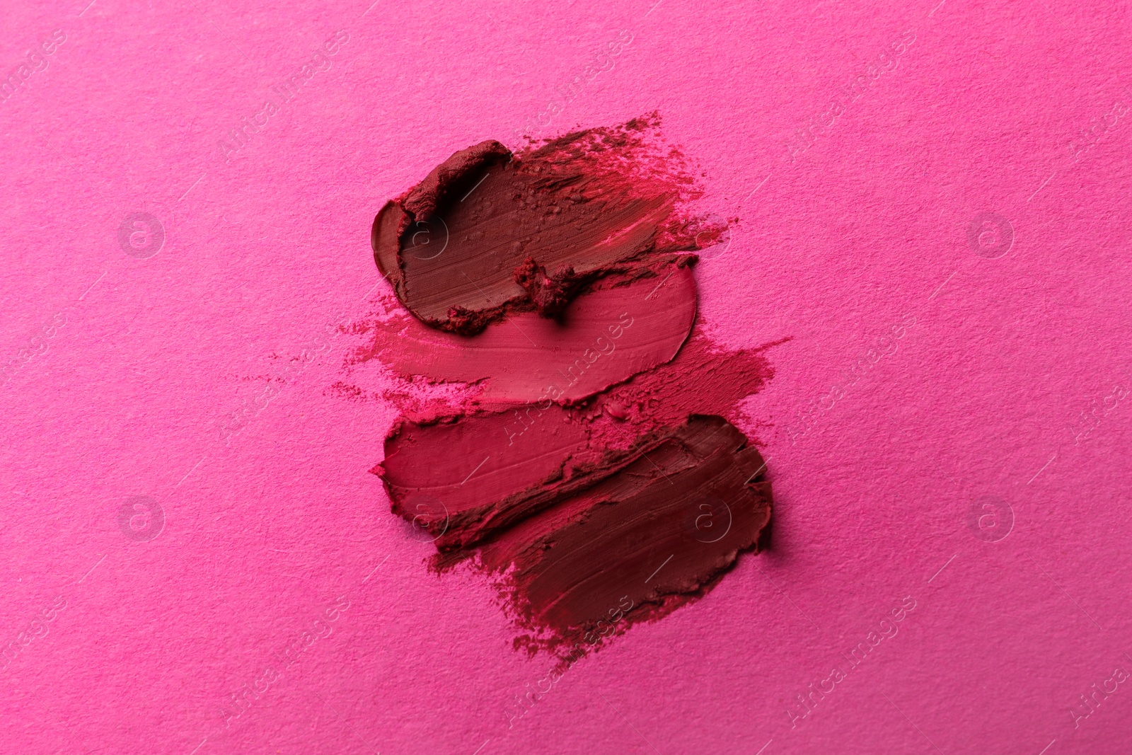 Photo of Smears of beautiful lipsticks on pink background, top view