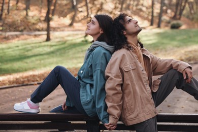 Photo of Young couple sitting on wooden bench in autumn park. Dating agency