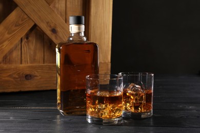 Whiskey with ice cubes in glasses and bottle on black wooden table