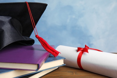 Graduation hat, books and student's diploma on wooden table against light blue background