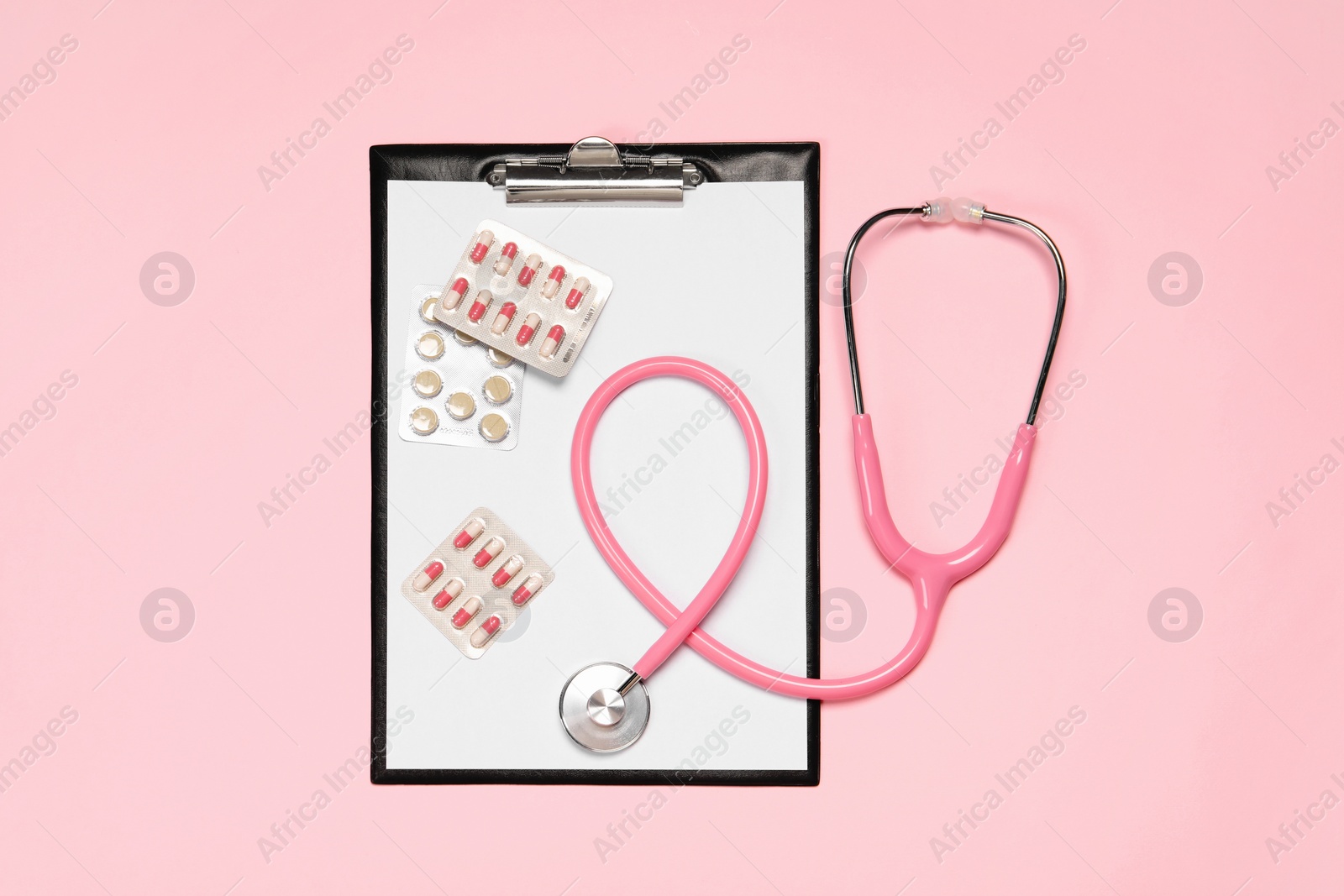 Photo of Stethoscope, clipboard and pills on pink background, top view. Medical tool