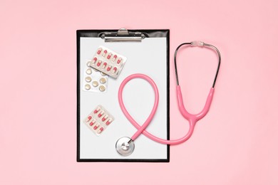 Stethoscope, clipboard and pills on pink background, top view. Medical tool