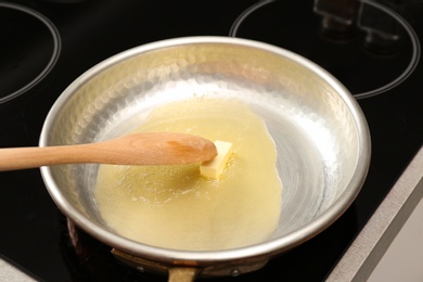 Frying pan with melted butter and wooden spoon on stove, closeup