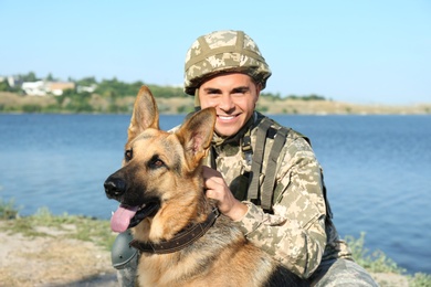 Photo of Man in military uniform with German shepherd dog near river