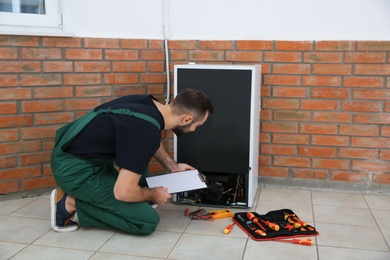 Male technician with clipboard examining refrigerator indoors