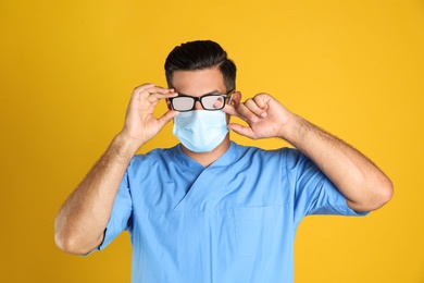 Photo of Doctor wiping foggy glasses caused by wearing medical mask on yellow background