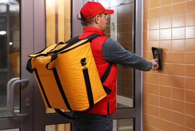 Photo of Male courier with thermo bag pushing intercom button. Food delivery service