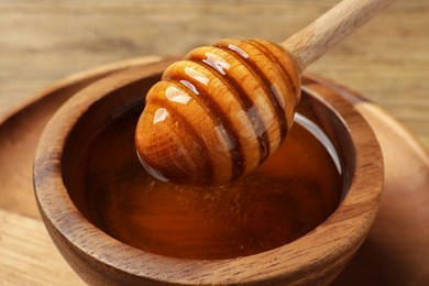 Photo of Dipper with honey in wooden bowl at table, closeup