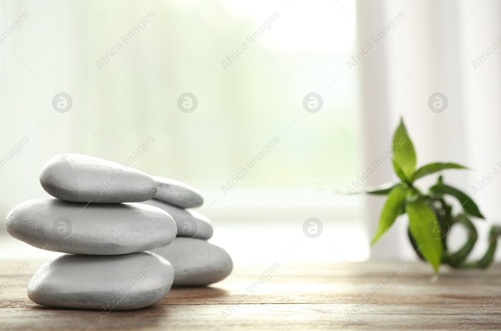 Photo of Spa stones and bamboo leaves on table against blurred background. Space for text