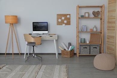 Photo of Stylish room interior with comfortable workplace and shelving unit near white wall