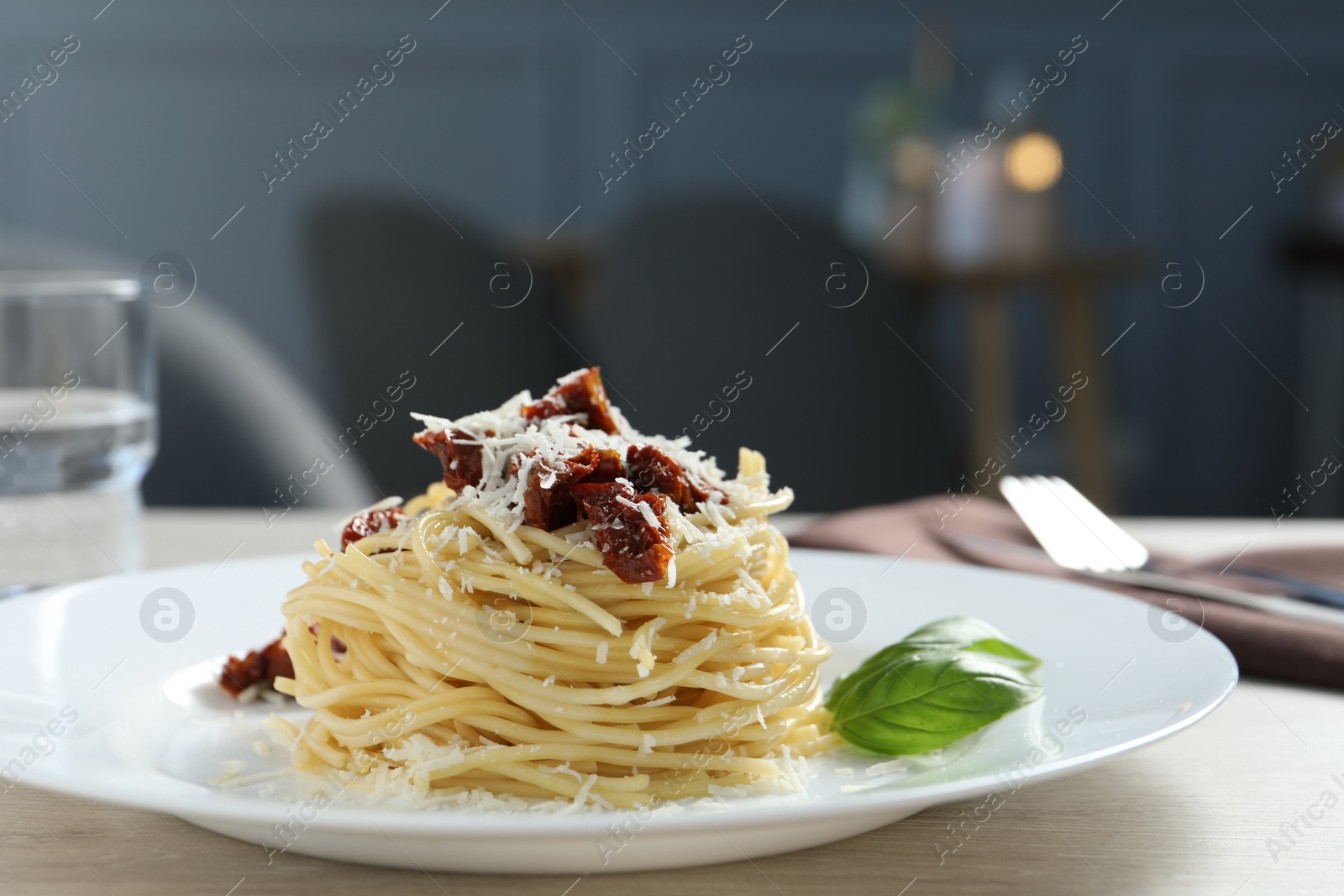 Photo of Tasty spaghetti with sun-dried tomatoes and parmesan cheese on wooden table in restaurant, closeup. Exquisite presentation of pasta dish