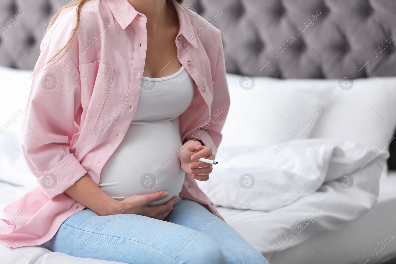 Photo of Young pregnant woman smoking cigarette in bedroom, closeup. Harm to unborn baby