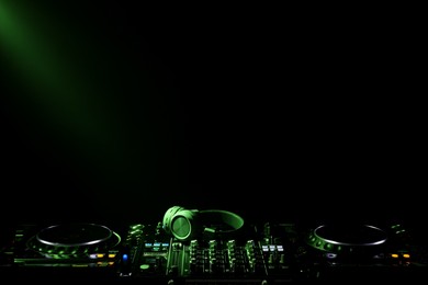 Modern DJ controller and headphones under beam of light on black background