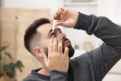 Photo of Young man applying medical eye drops indoors, closeup